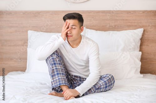 Young man suffering from sleep deprivation in bedroom