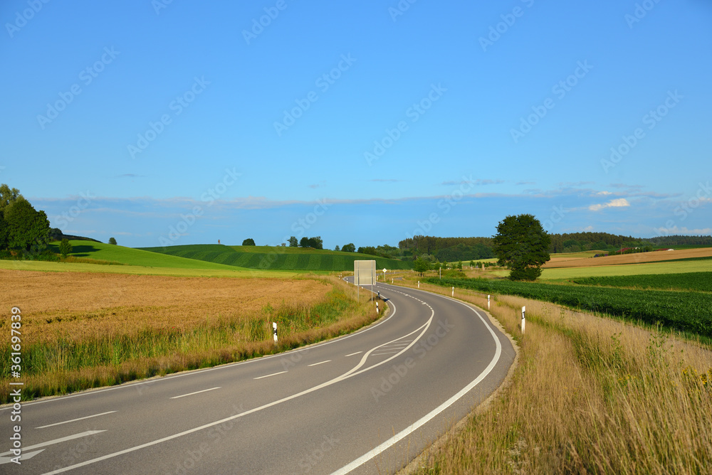 In Bavaria in summer a road leads through the fields and forests against a blue sky