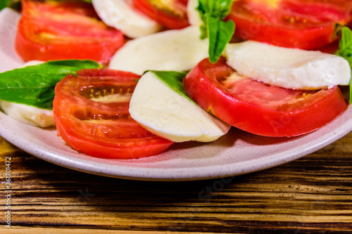 Plate with caprese salad (italian salad with cherry tomatoes, mozzarella cheese and basil leaves) on wooden table