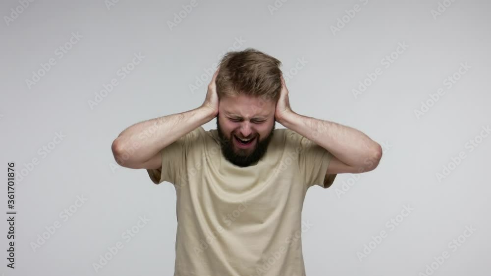 Depressed bearded man frustrated by loud noise covering ears clasping head, desperately saying No, want to stop unpleasant voices in mind, irritating sound. studio shot isolated on gray background Depressed bearded man frustrated by loud noise covering ears clasping head, desperately saying No, want to stop unpleasant voices in mind, irritating sound. studio shot isolated on gray background