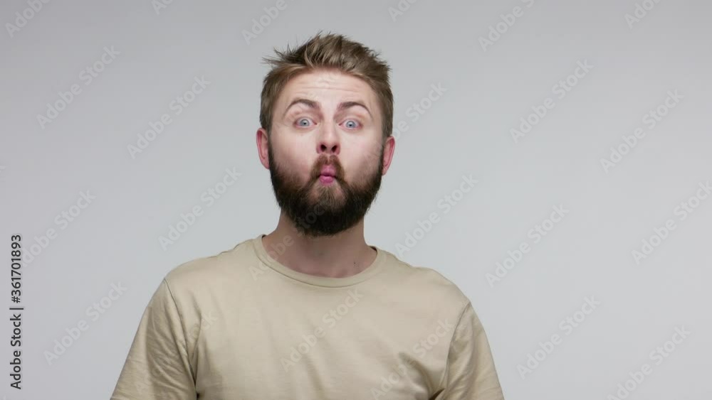 Surprised funny bearded guy looking at camera with surprised big eyes, making fish face grimace pout lips, smooching choking with idiotic duck expression. studio shot isolated on gray background Surprised funny bearded guy looking at camera with surprised big eyes, making fish face grimace pout lips, smooching choking with idiotic duck expression. studio shot isolated on gray background