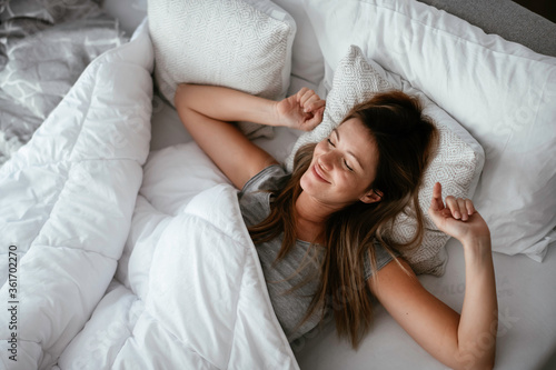 Woman stretching in bed after wake up. Beautiful girl enjoying morning light.