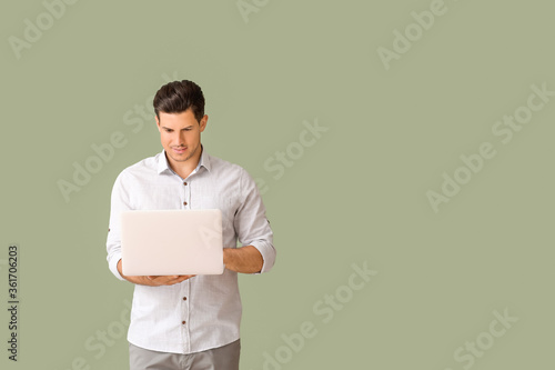 Young businessman in stylish shirt and with laptop on color background