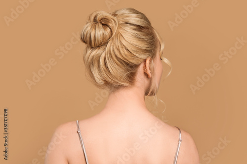 Beautiful young woman with stylish hairdo on color background, back view