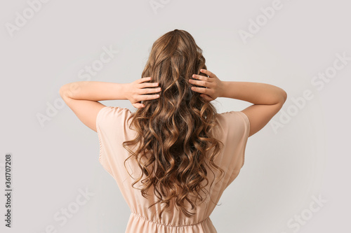 Beautiful young woman with stylish hairdo on grey background, back view