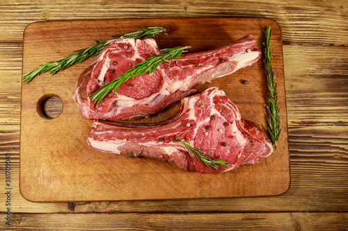 Raw fresh beef rib eye steaks on bone with spices and rosemary on wooden table. Top view