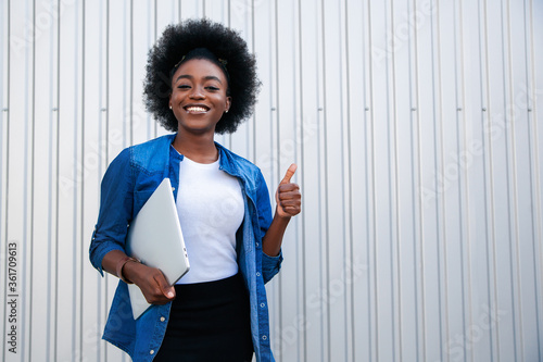 Image of a happy optimistic emotional young american african woman posing over grey background dressed in white casual, using laptop computer and showing thumbs up gesture.