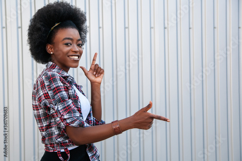 Promotion concept. Cheerful african american girl pointing aside on free space, recommending something. Grey background..