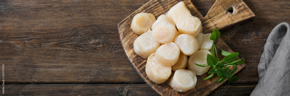 Scallops on a wooden Board on a brown wooden table. Scallops close-up. Top view with space for text. Banner