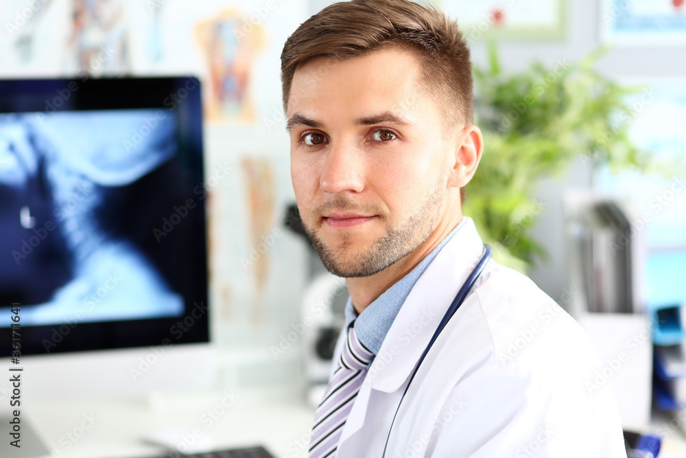 Portrait of smart physician sitting in clinic cabinet. Doc surgeon posing in white uniform. Medical treatment and healthcare concept. Blurred background Portrait of smart physician sitting in clinic cabinet. Doc surgeon posing in white uniform. Medical treatment and healthcare concept. Blurred background