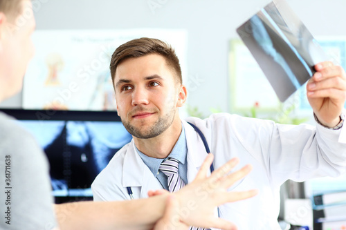 Portrait of smiling doctor talking with patient about good snapshot results. Doc looking at visitor with joyfulness. Medical and healthcare concept. Blurred background