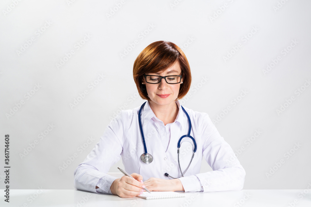 Adult redhead doctor writing on paper in office Adult redhead doctor writing on paper in office