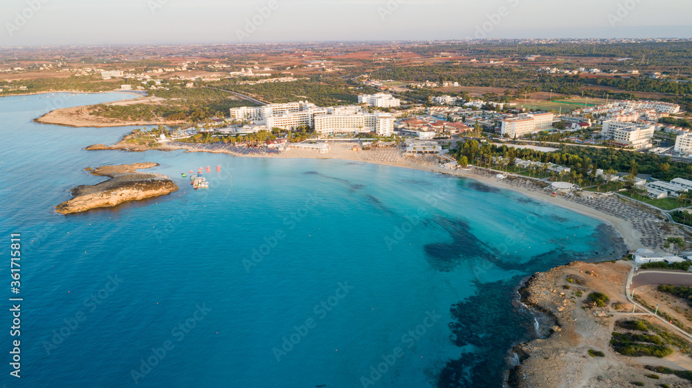 Aerial bird's eye view of famous Nissi beach coastline, Ayia Napa, Famagusta, Cyprus.Landmark tourist attraction islet bay at sunrise with golden sand, sunbeds, sea restaurants in Agia Napa from above