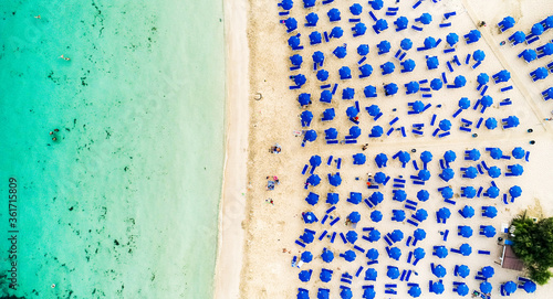 Aerial bird's eye view of Makronissos organised beach coastline, Ayia Napa, Famagusta, Cyprus from above. Blue aligned umbrellas, golden sand, parasols, people sunbathing sun beds clean turquoise sea. photo