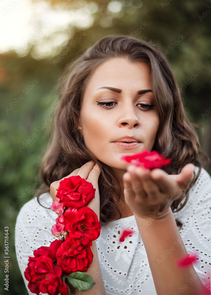Portrait of Beautiful girl in a white dress with roses on her hand blows off the petals from the palm. Portrait of Beautiful girl in a white dress with roses on her hand blows off the petals from the palm.