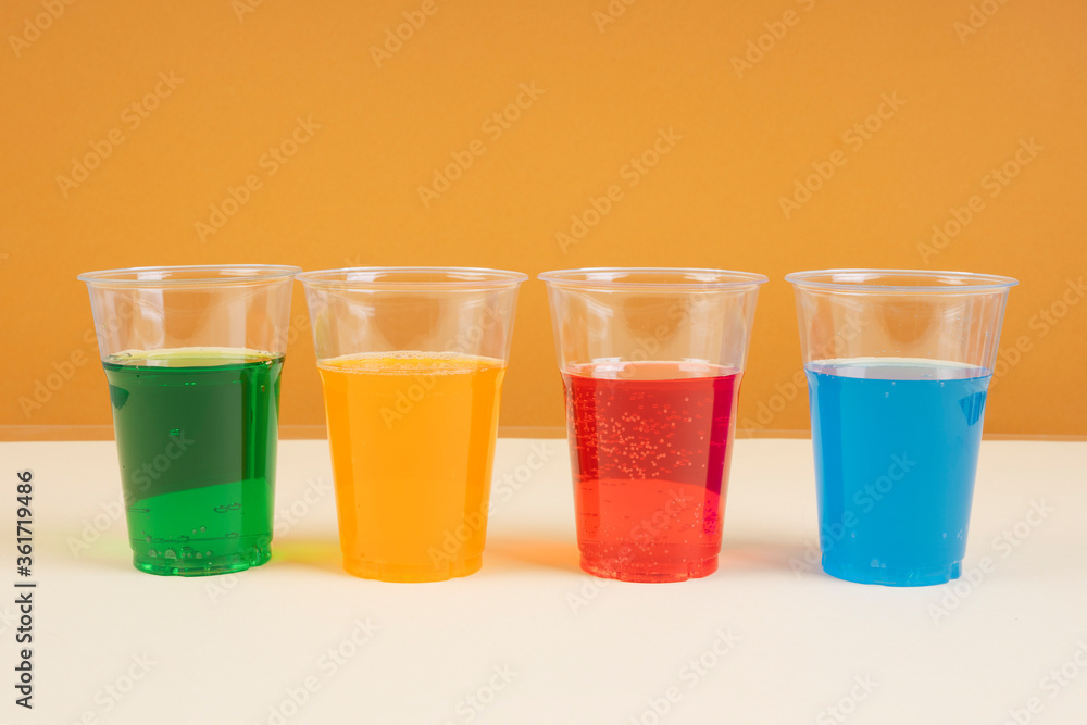 Sweet rainbow soda sparkling water in plastic cup with copy space. Green. Blue. Orange. Red. Sweet rainbow soda sparkling water in plastic cup with copy space. Green. Blue. Orange. Red.