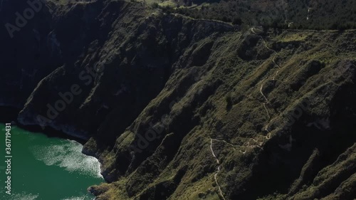 Aerial view of the Quilotoa lake in Ecuador, showing the side of the lake and a trail going down the crater
