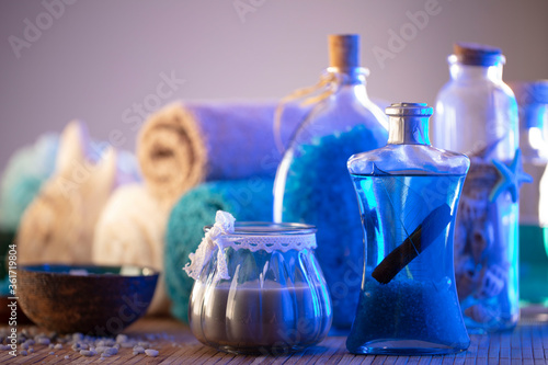 Spa and wellness concept. Bottles with cosmetics, rolled up towels, bath salts and care products on wooden paneling.