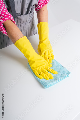 Maid woman wearing gloves cleaning dinning table with cloth rag. Covid-19 Coronavirus prevention. photo