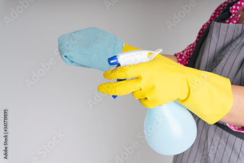 Maid wearing protective yellow gloves holding rag cloth and detergent spray bottle.