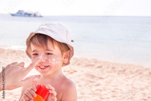 Hand of caucasian mother applying suncream  to her son on beach.