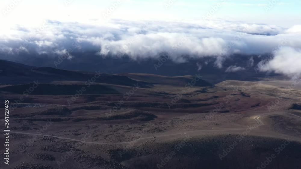 Stunning aerial view of a moving cloudscape with thick white clouds over a dark large and empty plain with a deserted dirt road
