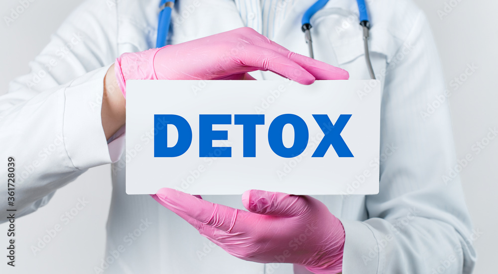 Cropped view of young female doctor in a white coat and pink sterile gloves holding a card with text DETOX. Medical concept. Cropped view of young female doctor in a white coat and pink sterile gloves holding a card with text DETOX. Medical concept.