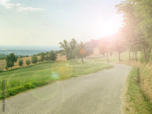 Typical Italian country side winding road on a beautiful summer day.  Colli piacentini hills near Piacenza in Emilia Romagna, Italy. Sunshine creating lens flares.  photo