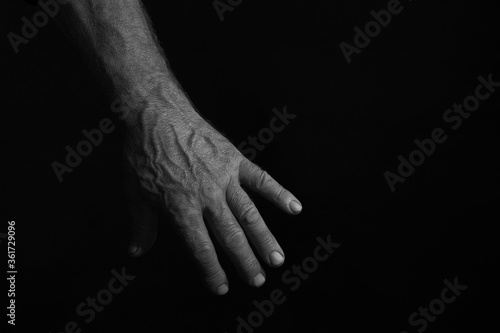 A man's, manly hand against a black background. The photo is in a low key. Horizontal.