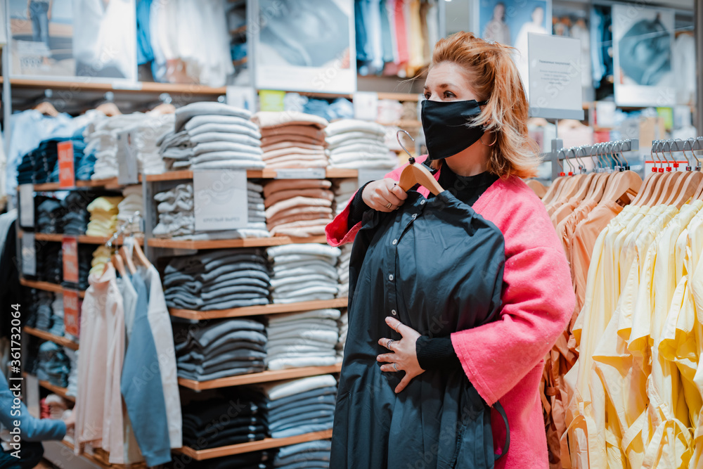beautiful woman with phone bright pink shopping Mall coat with black protective mask on her face from virus infected air.