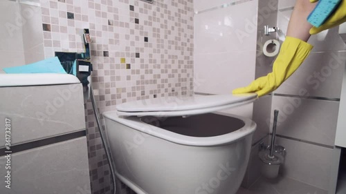 Having washed toilet girl closes lid of toilet and wipes it with cleaning cloth.