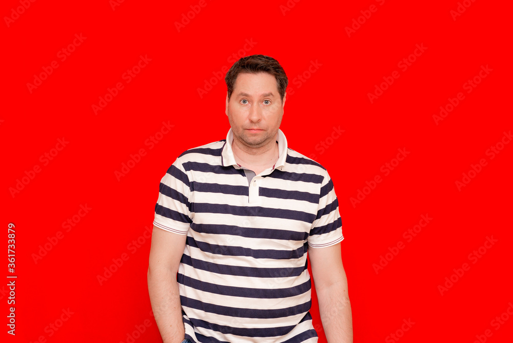 Irritated man 35 40s in striped t-shirt standing look isolated over red background Irritated man 35 40s in striped t-shirt standing look isolated over red background