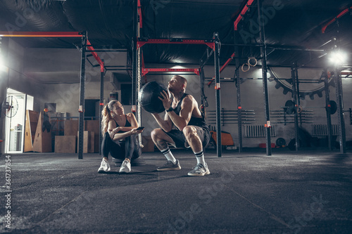 Beautiful young sporty couple workout in gym together. Caucasian man training with female trainer. Concept of sport, activity, healthy lifestyle, strength and power. Working out with ball.