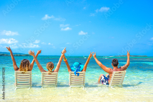 group of young friends on caribbean pristine beach with arms up, enjoying and sharing summer holidays, boys and girls celebrating life together photo