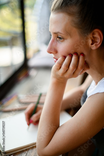 portrait of beautiful woman who props her head with her hand and looks out the window.