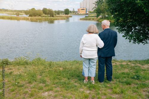 The older man and woman stand with their backs against the backdrop of the blue lake. ©  drugoenebo