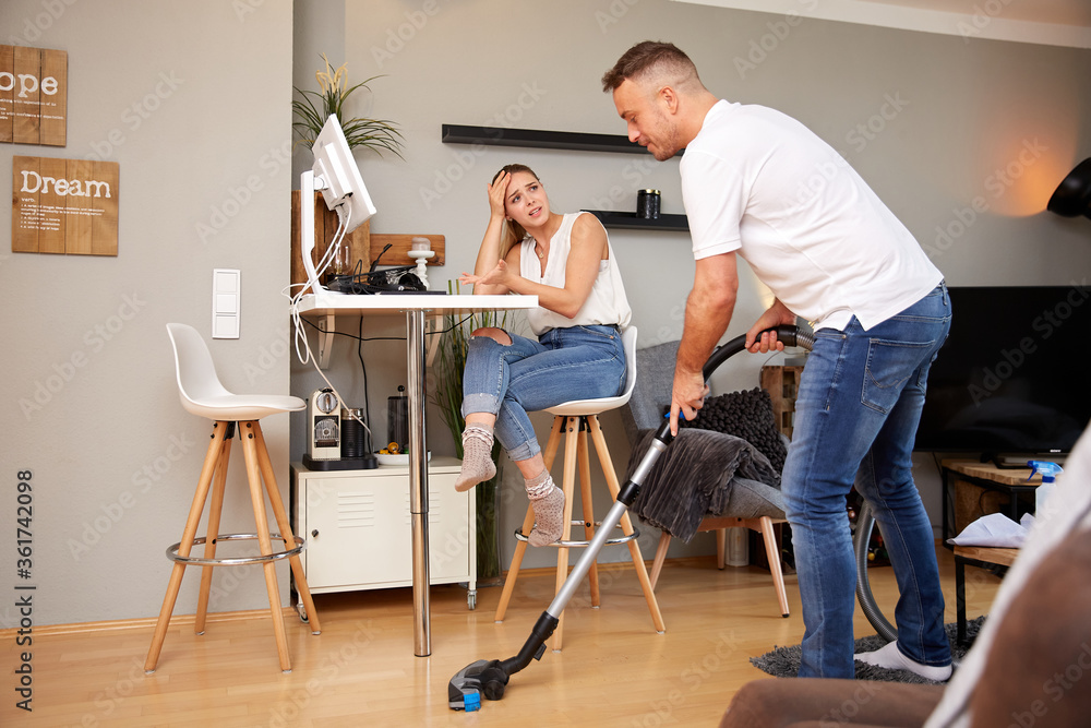 Frustrated Businesswoman Looking At Man Using Vacuum Cleaner