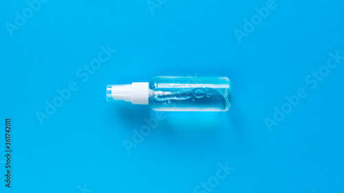 Hand sanitizer transparent bottle with spray cap at the middle of blue background. Simple flat lay with pastel paper texture. Medical concept. Stock photo.