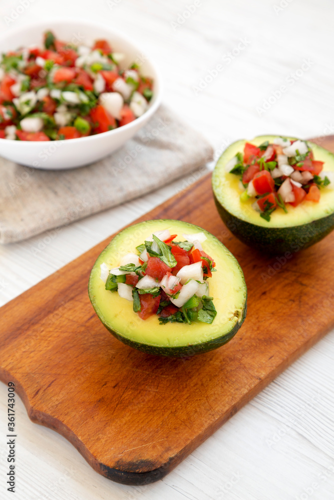 Homemade Pico de Gallo Stuffed Avocado on a rustic wooden board on a white wooden surface, low angle view. Homemade Pico de Gallo Stuffed Avocado on a rustic wooden board on a white wooden surface, low angle view.