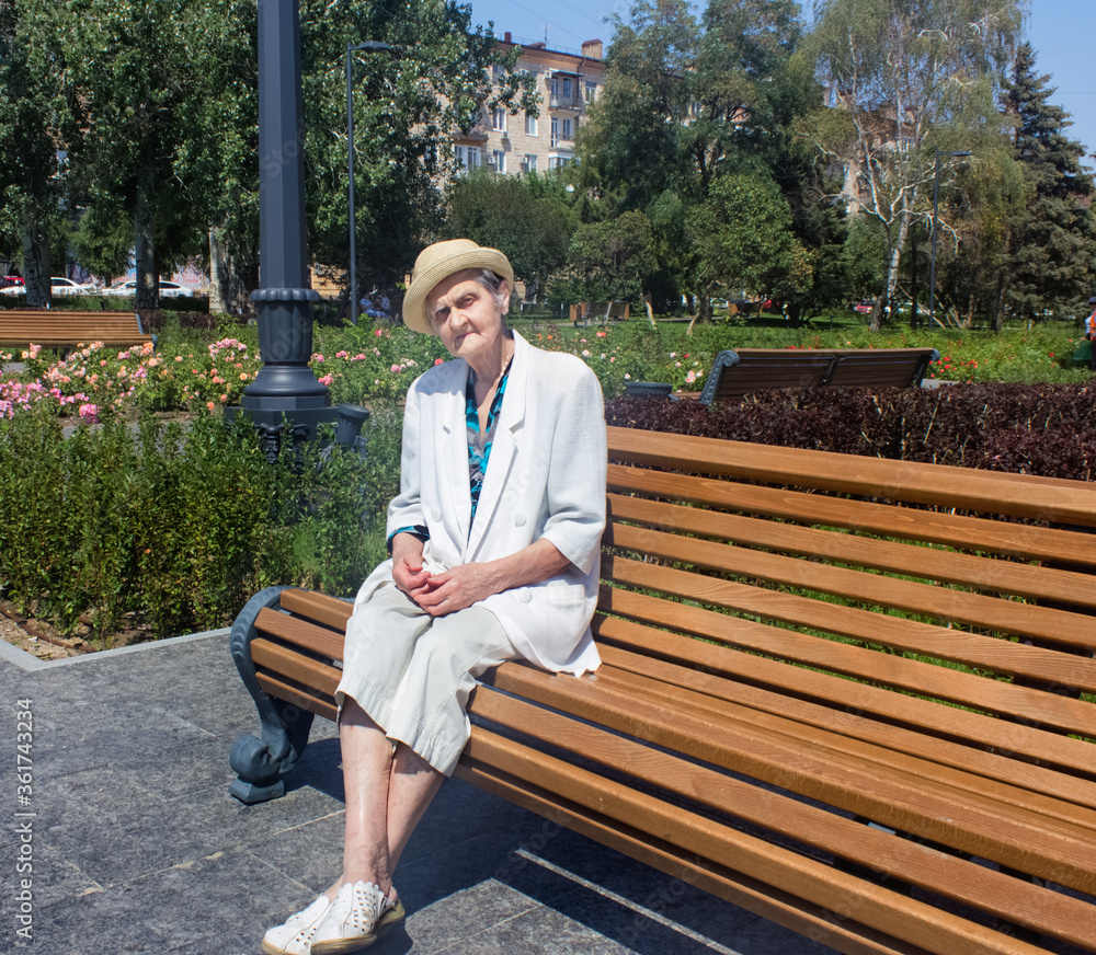 Elderly woman taking a walk. Senior woman in straw hat on a park bench. Social distance.