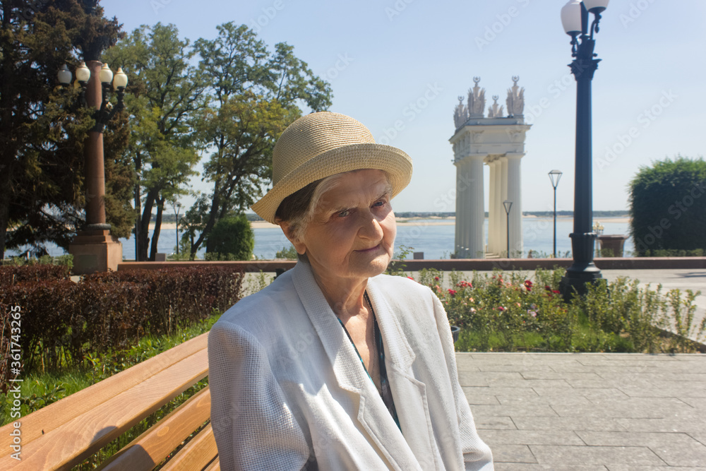 Elderly woman taking a walk. Senior woman in straw hat on a park bench. Social distance.