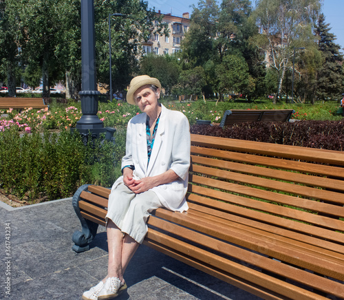 Obraz na płótnie Elderly woman taking a walk. Senior woman in straw hat on a park bench. Social distance. w salonie