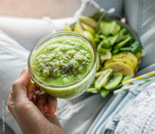 Woman in jeans holding fresh green smoothie with sesame, kiwi, apple, cucumber on light background. Healthy food, clean eating, detox, close up