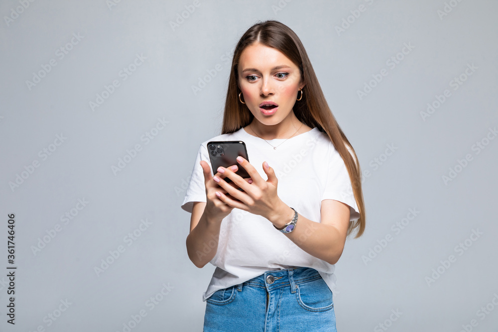 Exciting woman reading text message on the phone isolated on gray background Exciting woman reading text message on the phone isolated on gray background