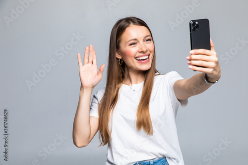 Happy young woman blogger influencer holding modern smart phone wave hand hello. Smiling vlogger girl looking at mobile make video call, shooting vlog taking selfie isolated on grey background