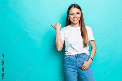 Trendy attractive young woman wearing mustard color summer dress posing over pastel blue background. Front view of smiling woman pointing with finger and looking to her right.