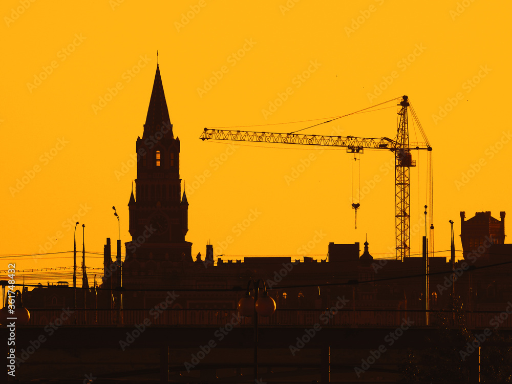 Naklejka premium Silhouettes of lifting cranes and city tower at the yellow sky in Yoshkar-Ola city, Mari El, Russian Federation