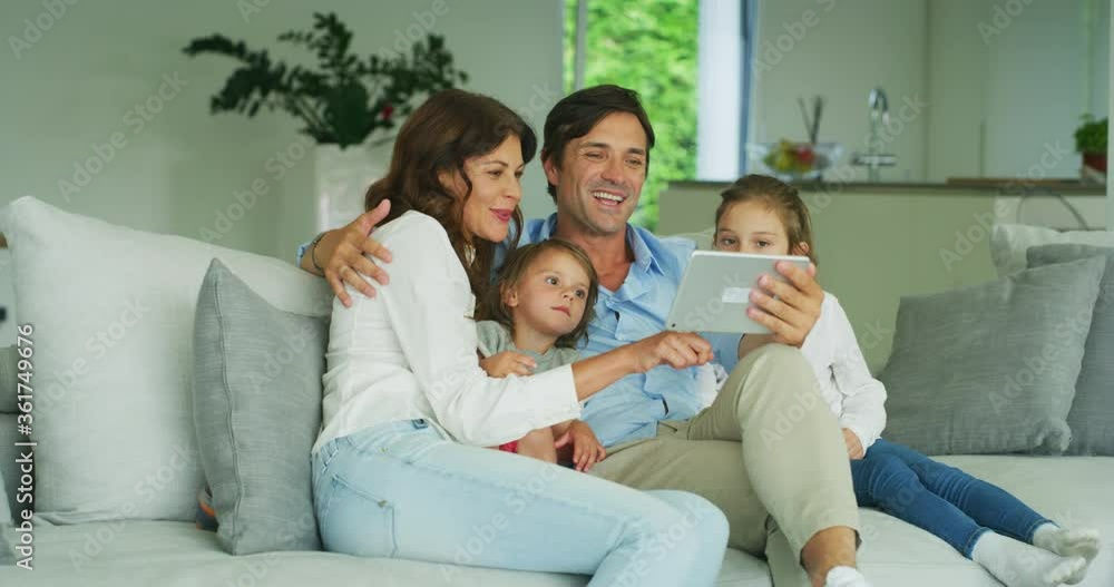 Happy smiling parents with kids are having fun using a technology tablet for family entertainment or education on a sofa in living room. Happy smiling parents with kids are having fun using a technology tablet for family entertainment or education on a sofa in living room.