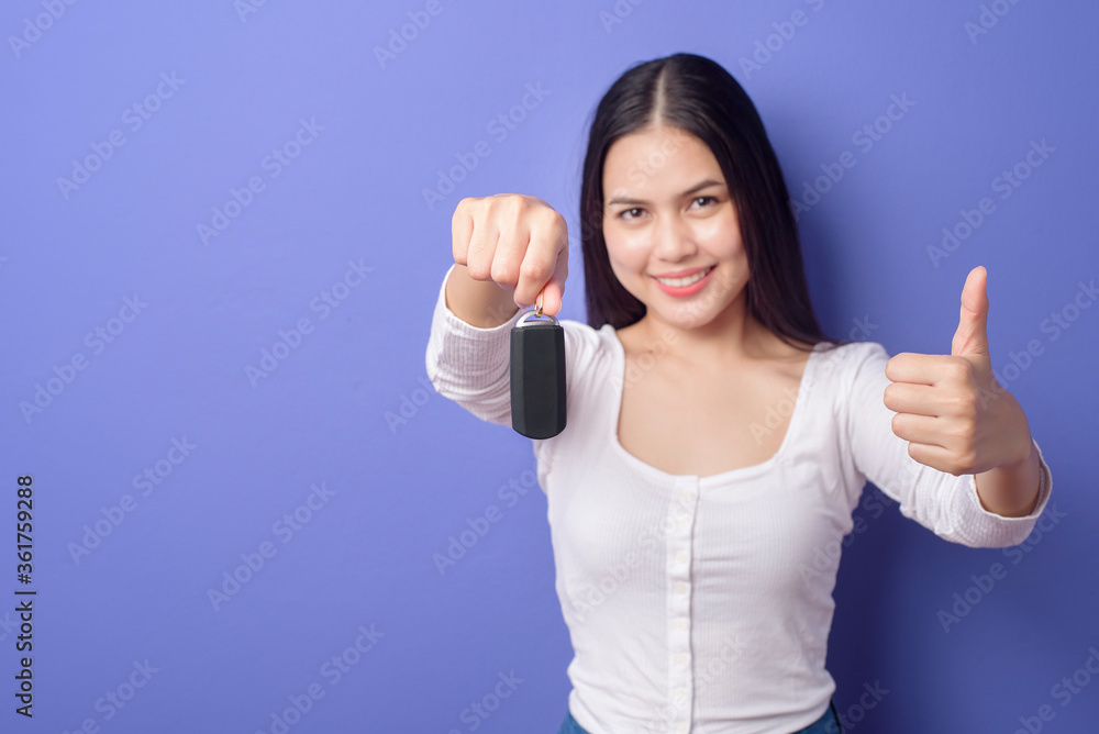 Fototapeta premium Young beautiful smiling woman is holding car key over isolated purple background studio