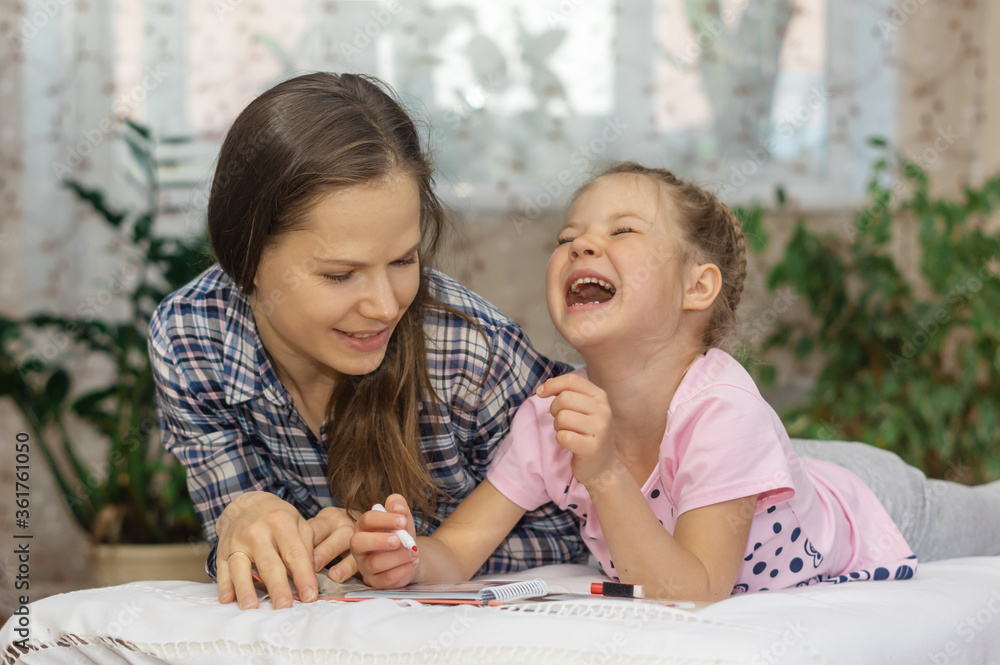 Mother and daughter together are engaged in joint activities, solve Sudoku puzzles (crosswords) at home on the bed (sofa) and smile (laugh). Concept of parents and children spending time together.